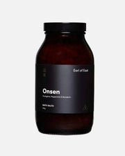 A dark amber glass jar of Earl of East Onsen bath salts with a black lid and a black label, shown on a clean white background.