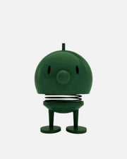 A dark green robot-shaped spring toy with a round head, small eye cutouts, a circular nose, a coiled spring between the head and legs, and two round feet, shown on a plain white background.