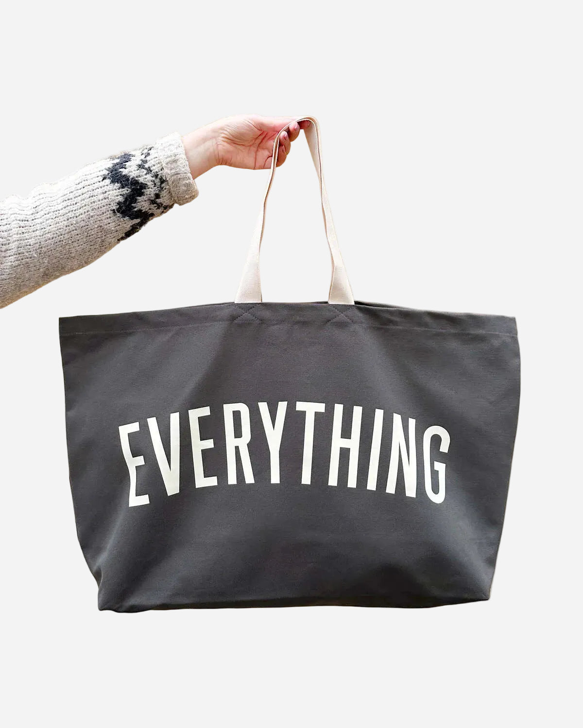 Black tote bag with 'EVERYTHING' text held by a person against a beige background