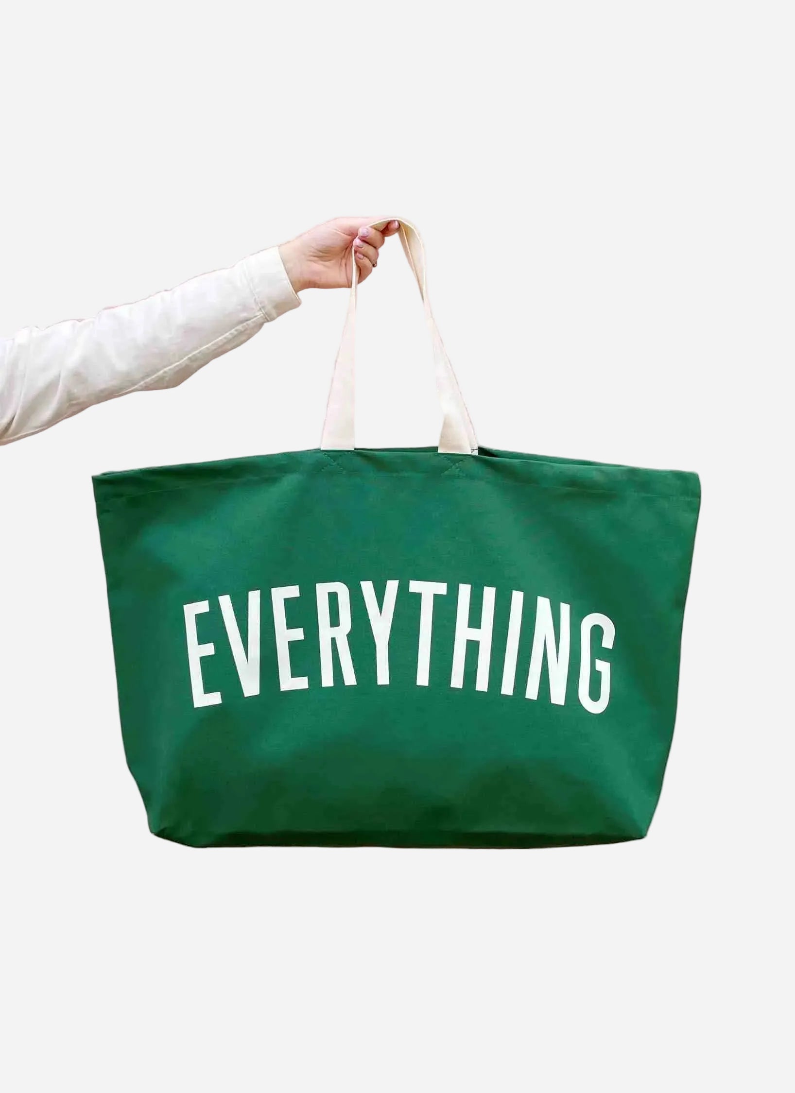 Green tote bag with 'EVERYTHING' text held by a person on a white background