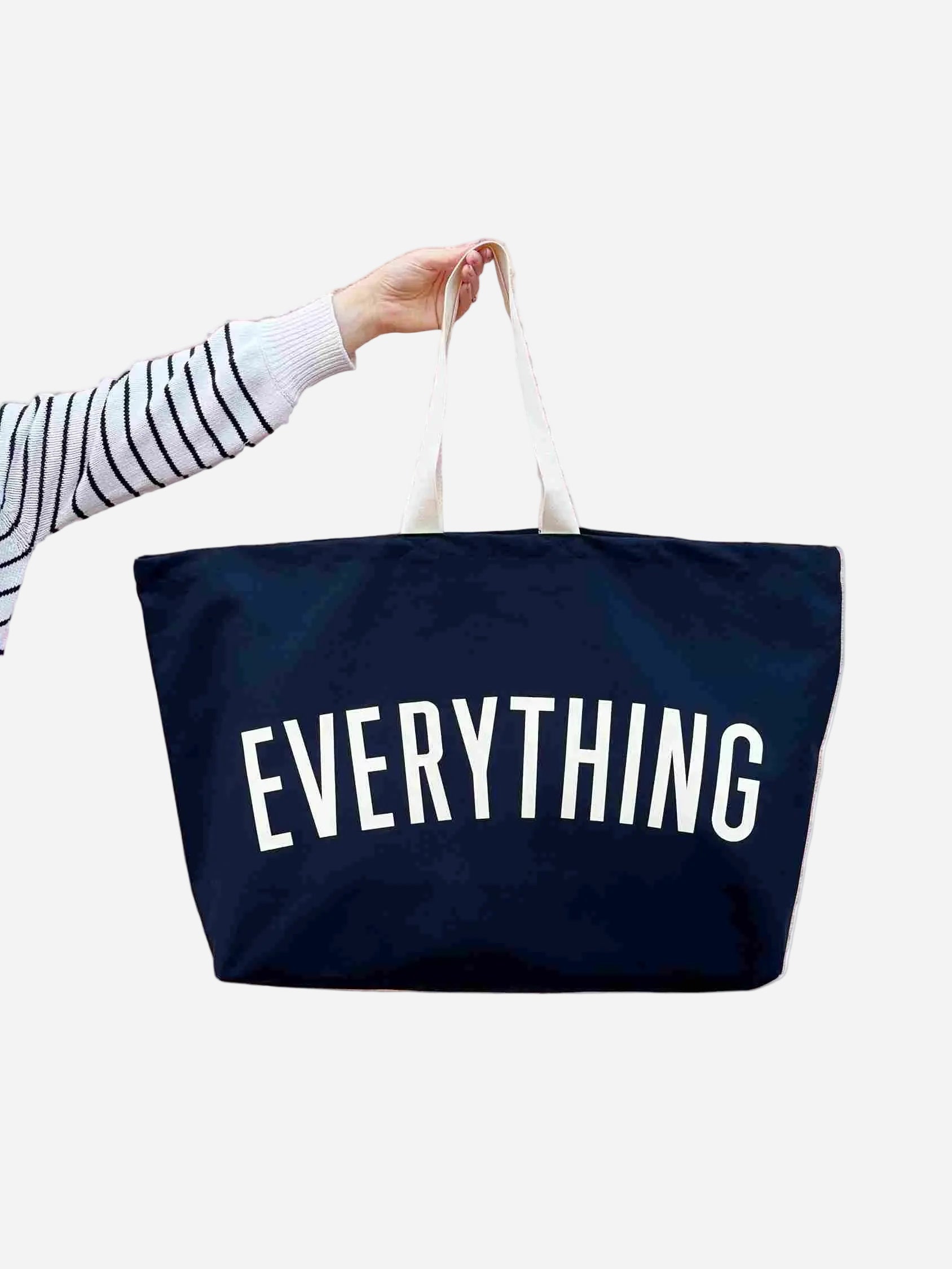 Navy tote bag with 'EVERYTHING' text held by a person on a white background