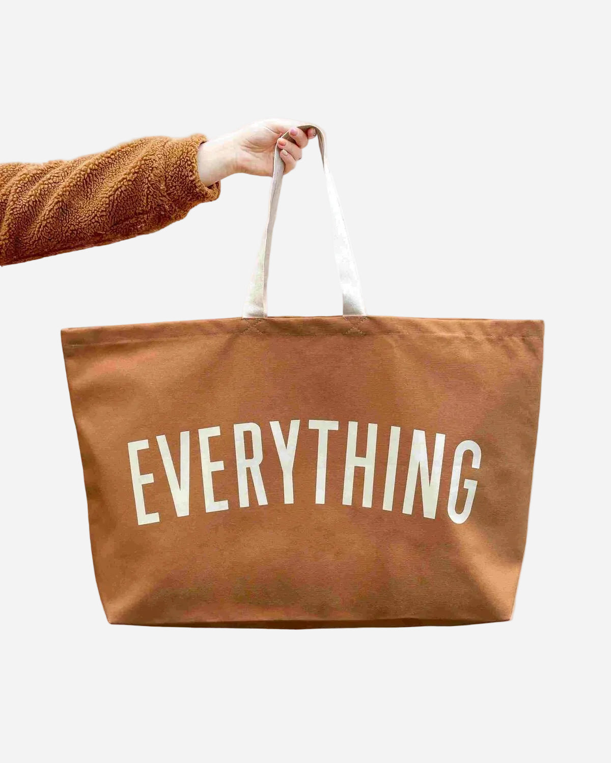Brown tote bag with 'EVERYTHING' text held by a person against a pink background